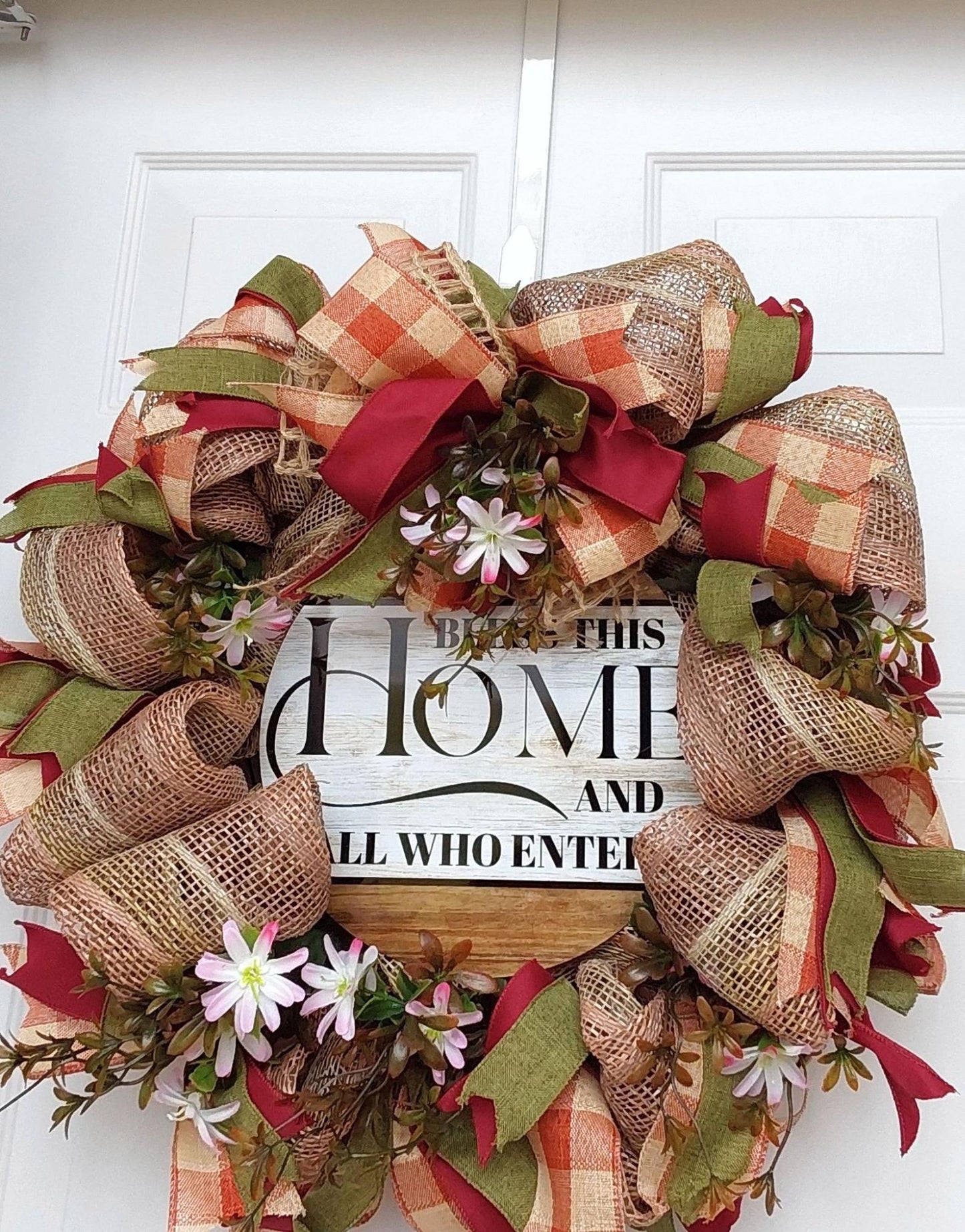 A wreath of ribbon, flowers and burlap with "Bless this Home and all who enter" at the center