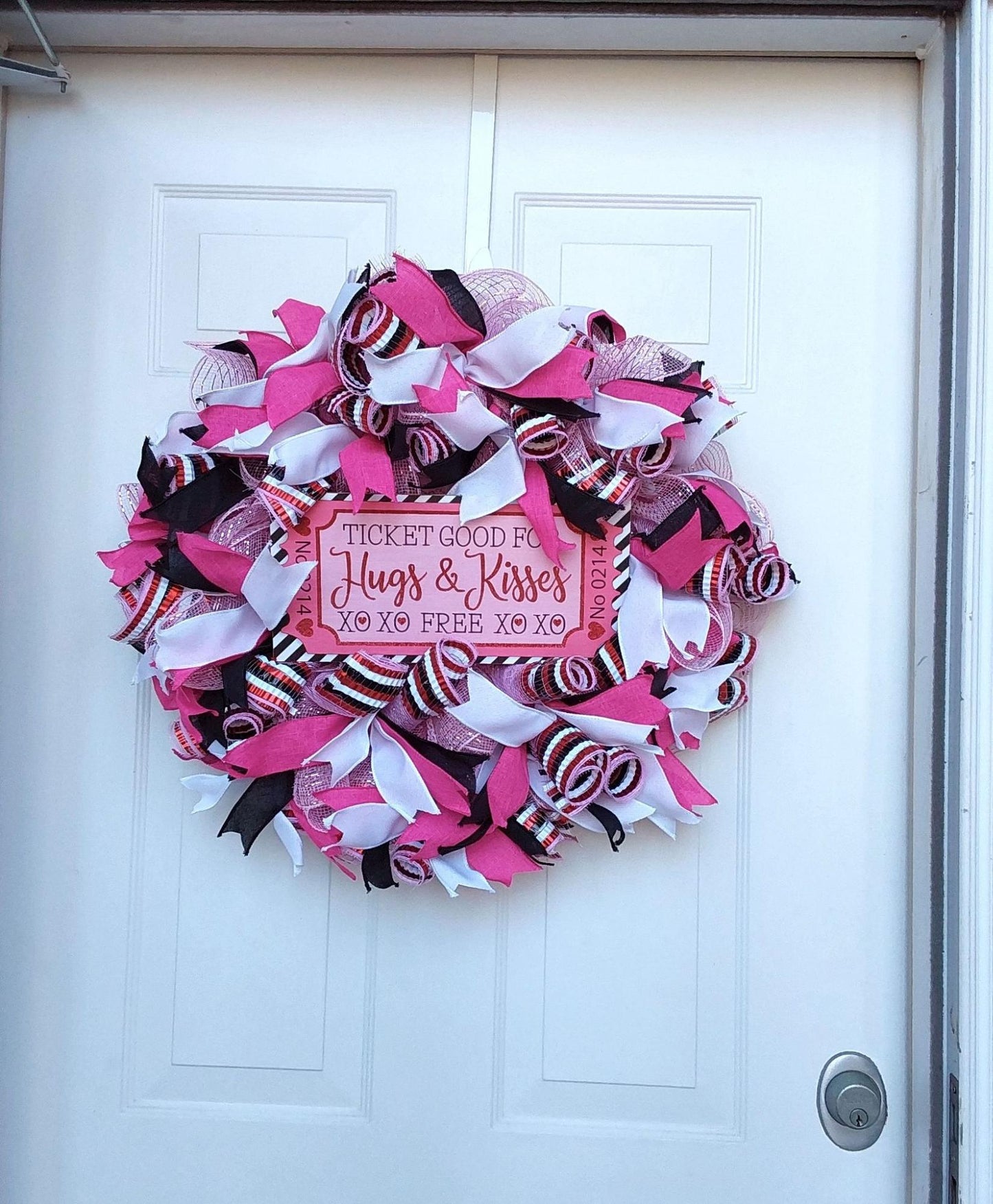 Pink and white ribbons on a wreath with a "Ticket Good for Hugs & Kisses" centerpiece.