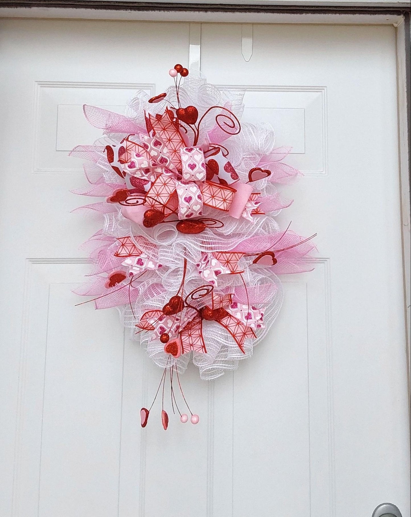 Teardrop wreath with a Valentine's theme in pink, white, and red ribbons and mesh.