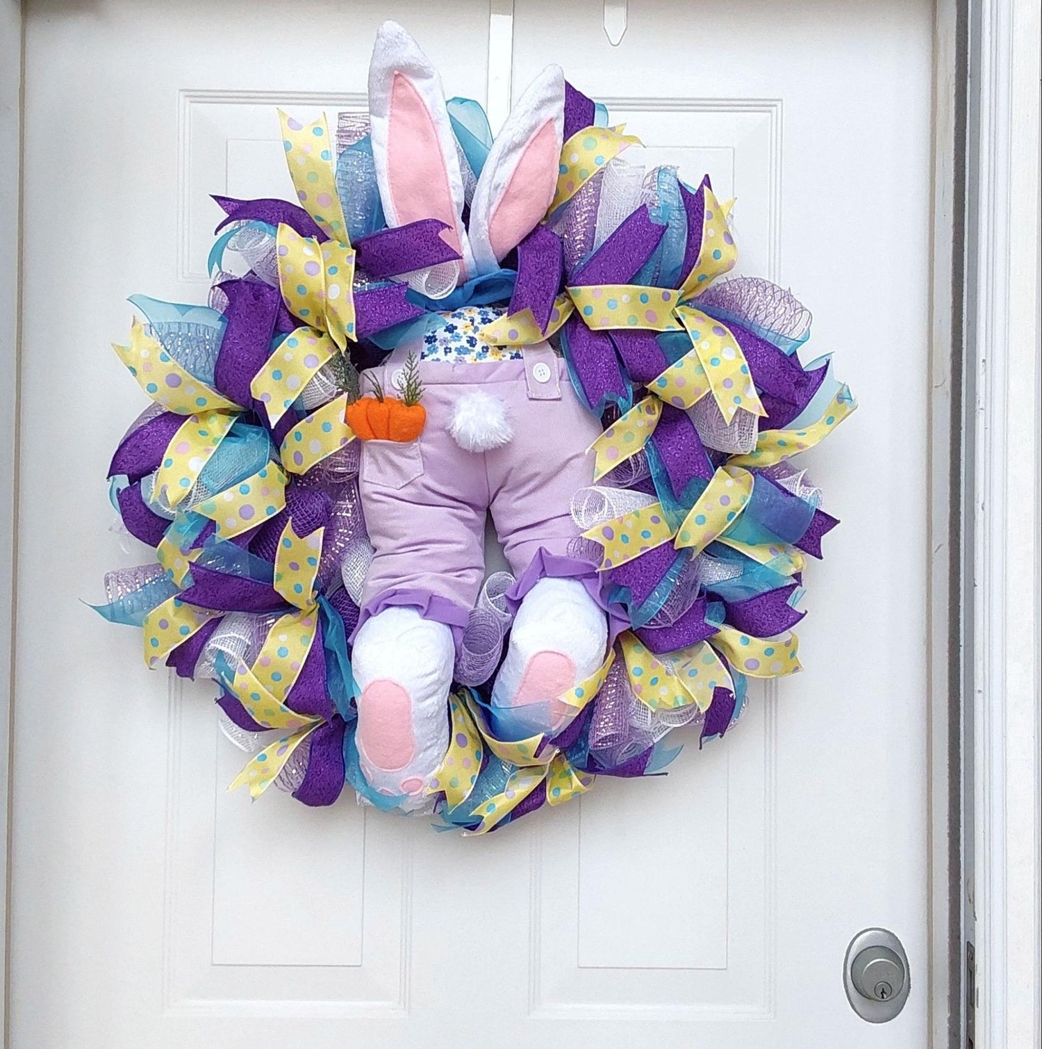 A wreath hanging on a door with a bunny butt and ears at the center