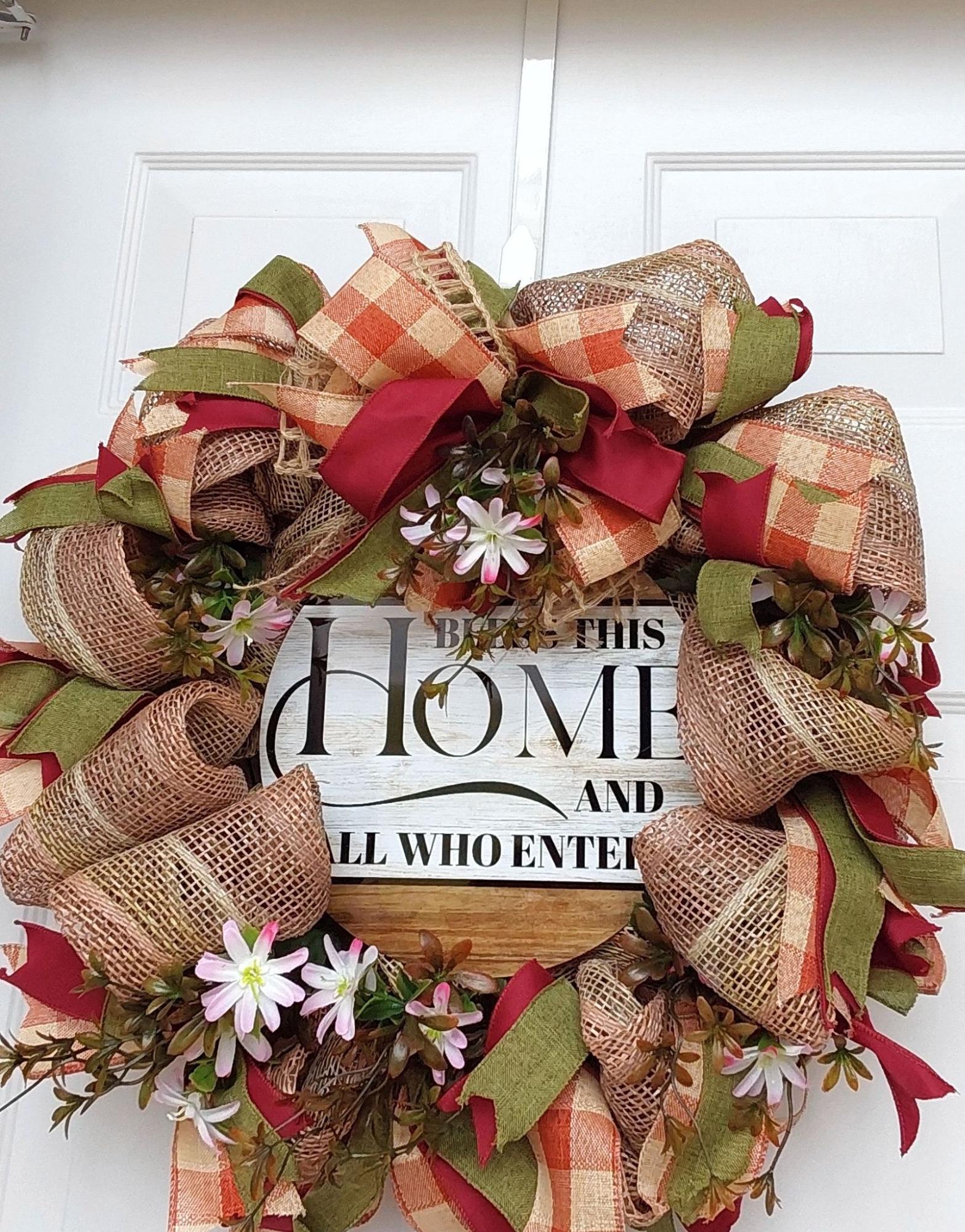 A wreath of ribbon, flowers and burlap with "Bless this Home and all who enter" at the center