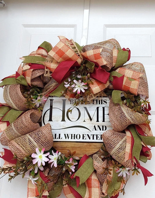 A wreath of ribbon, flowers and burlap with "Bless this Home and all who enter" at the center