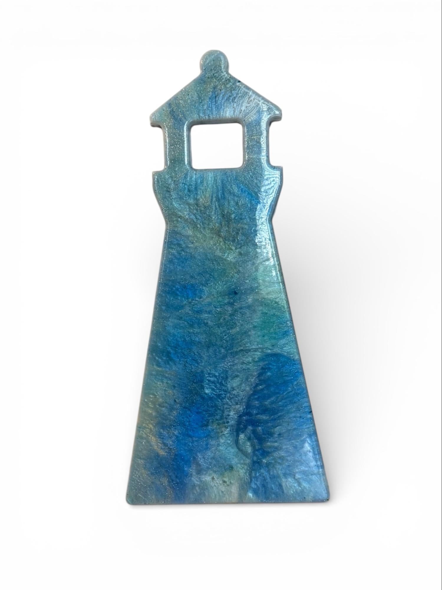A resin wall art in the shape of a lighthouse in deep blue, teal, and soft seafoam.