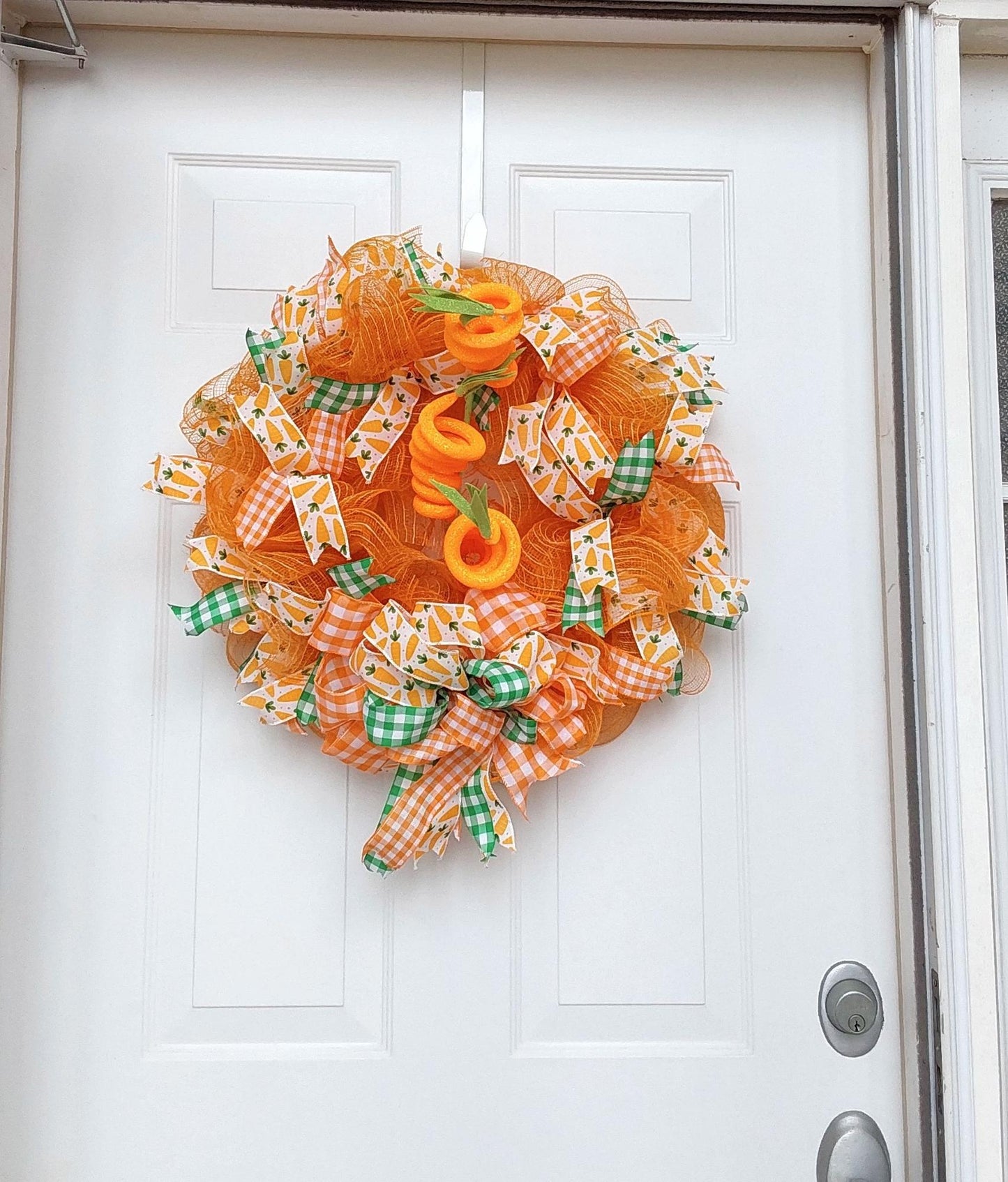 An orange and green Easter wreath with carrot embellishments hanging on a door.