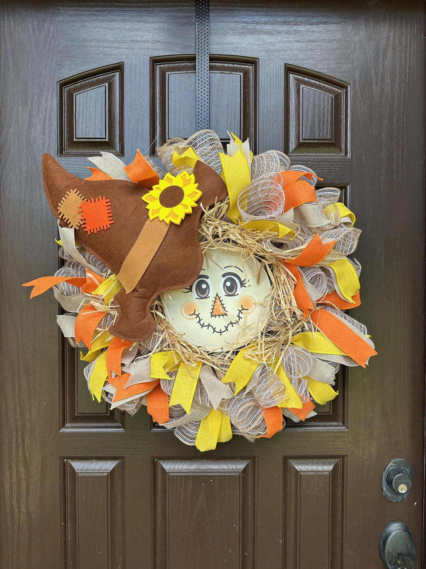 A scarecrow face at the center of a ribbon wreath with a brown hat.