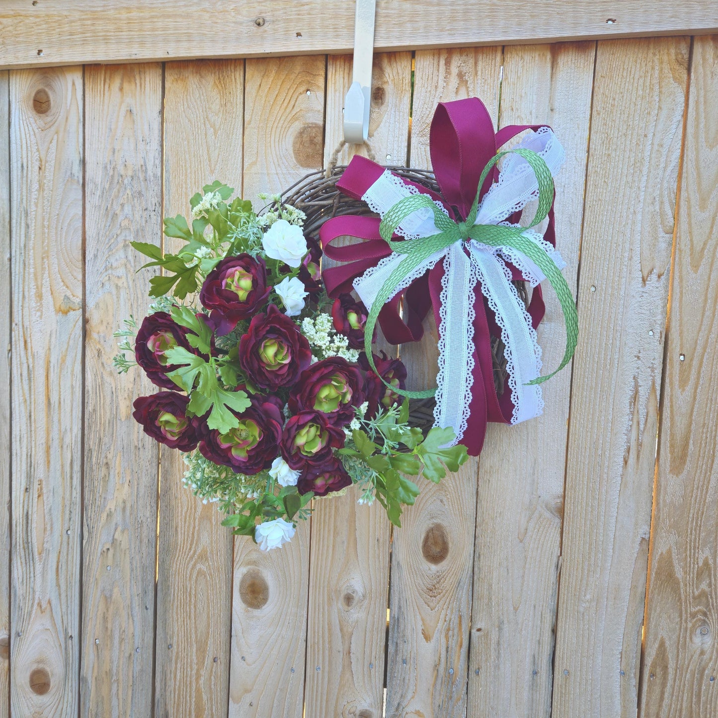 A wreath with ribbon bows and roses on a fence.