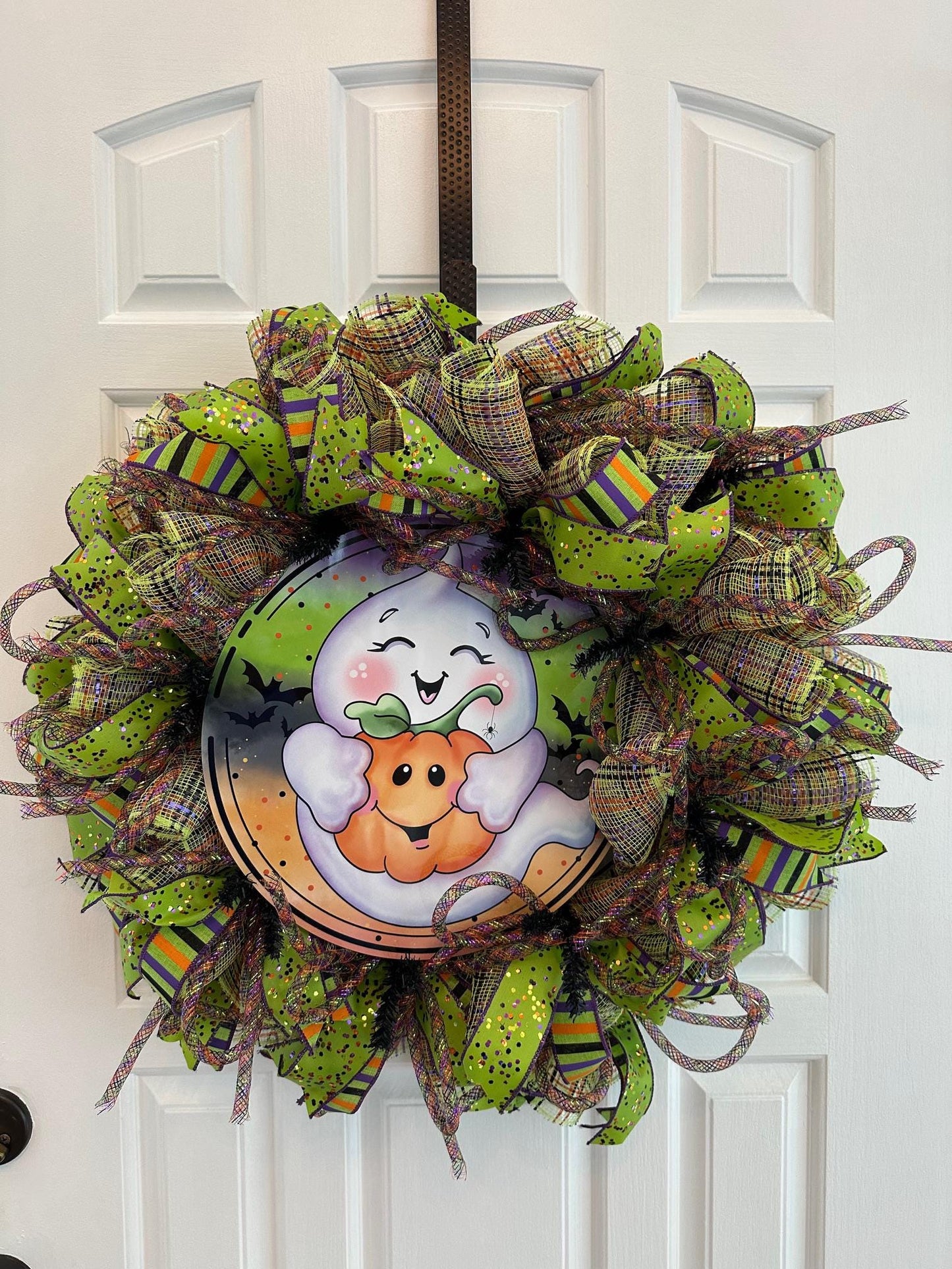 A cute ghost hugging a pumpkin n the middle of a green, orange, and purple ribboned wreath.