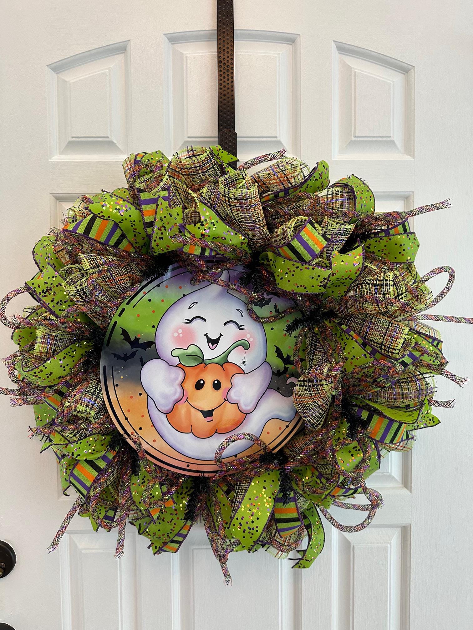 A cute ghost hugging a pumpkin n the middle of a green, orange, and purple ribboned wreath.
