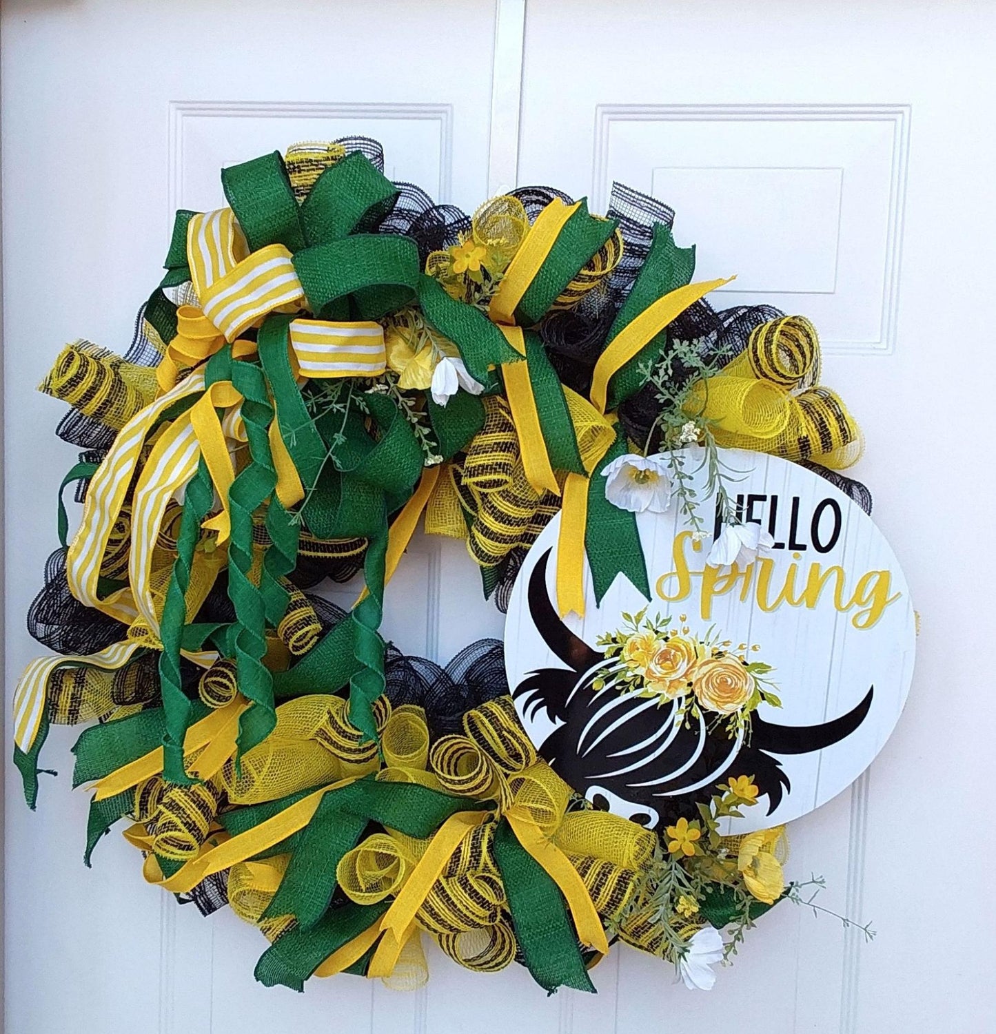 Bold green and yellow ribbons on a wreath with a "Hello Spring" centerpiece featuring a highland cow