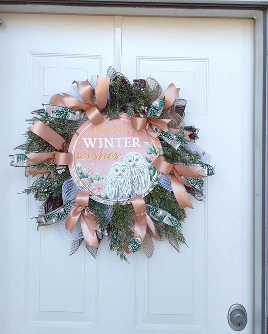 Pink ribbons and greenery on a wreath with a "Warm winter wishes" centerpiece with snow owls