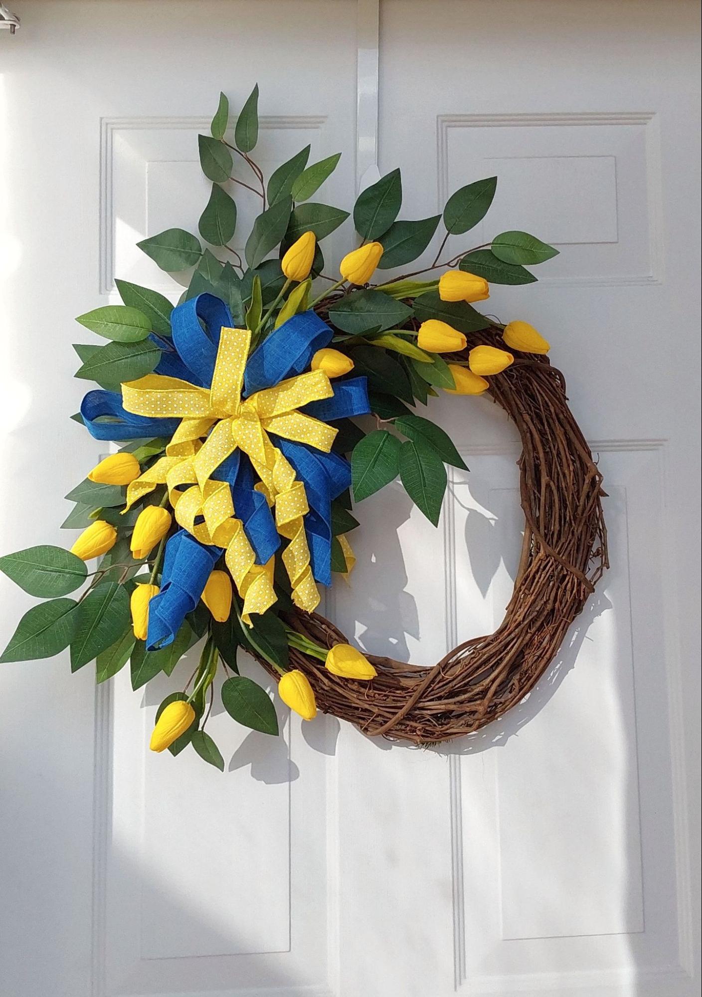 A door wreath with yellow and blue ribbons and yellow tulips.